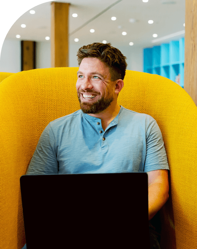 Man sitting on yellow couch with laptop smiling