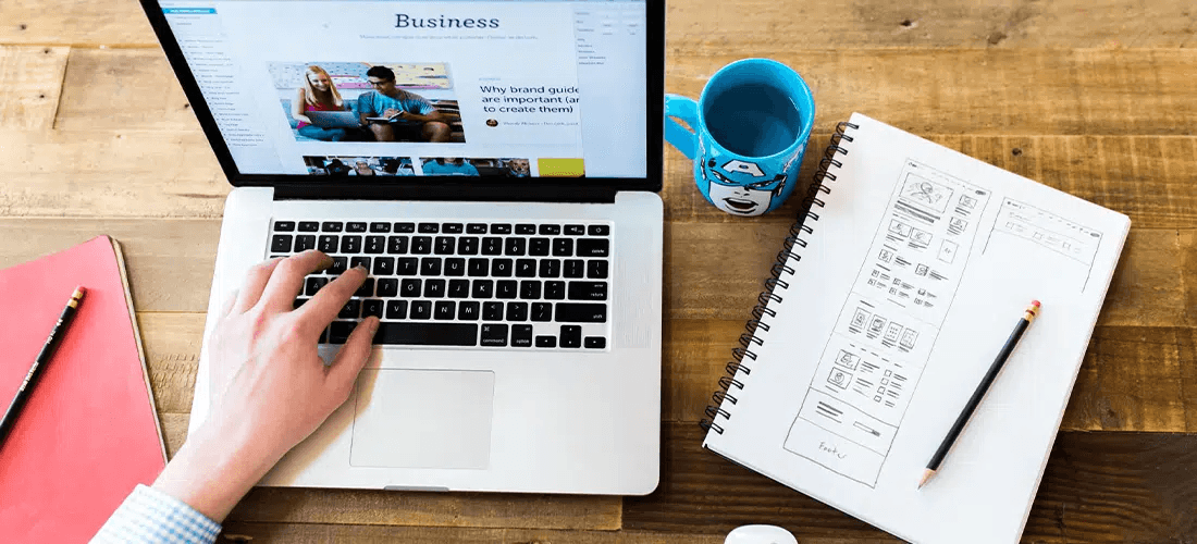 Hand typing on laptop with pen and paper