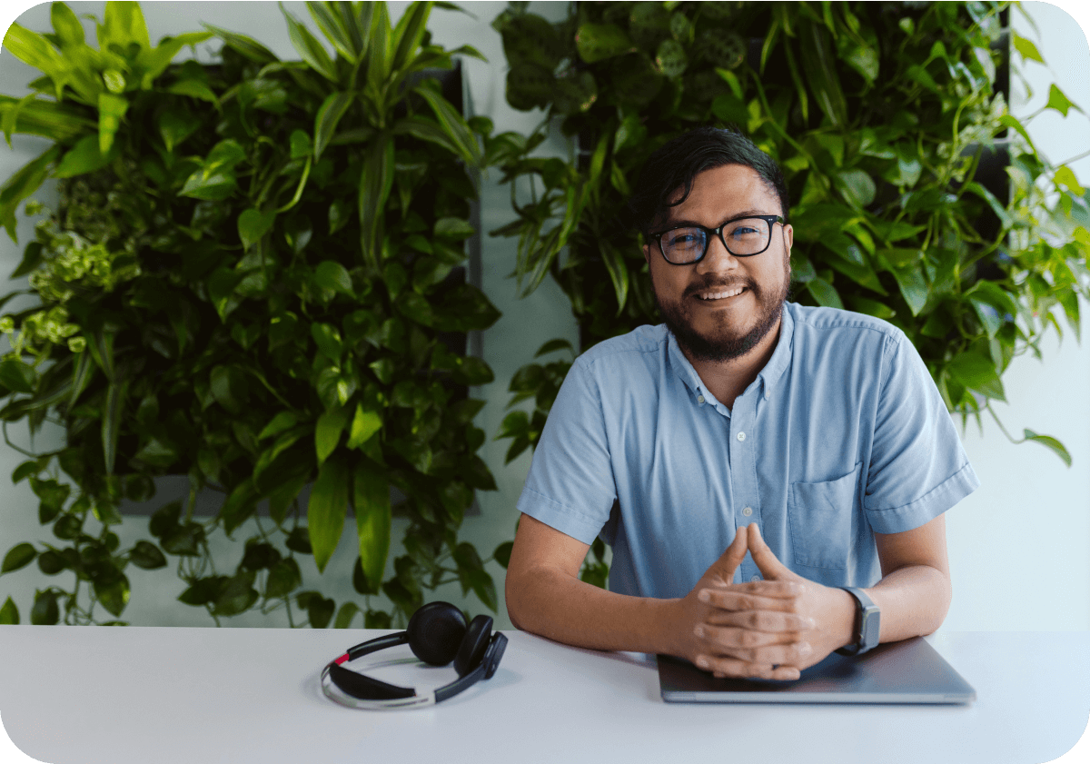 man sitting at a table with a closed laptop and headphones in front of a wall of plants