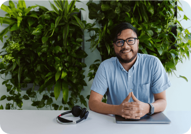 man sitting at a table with a closed laptop and headphones in front of a wall of plants
