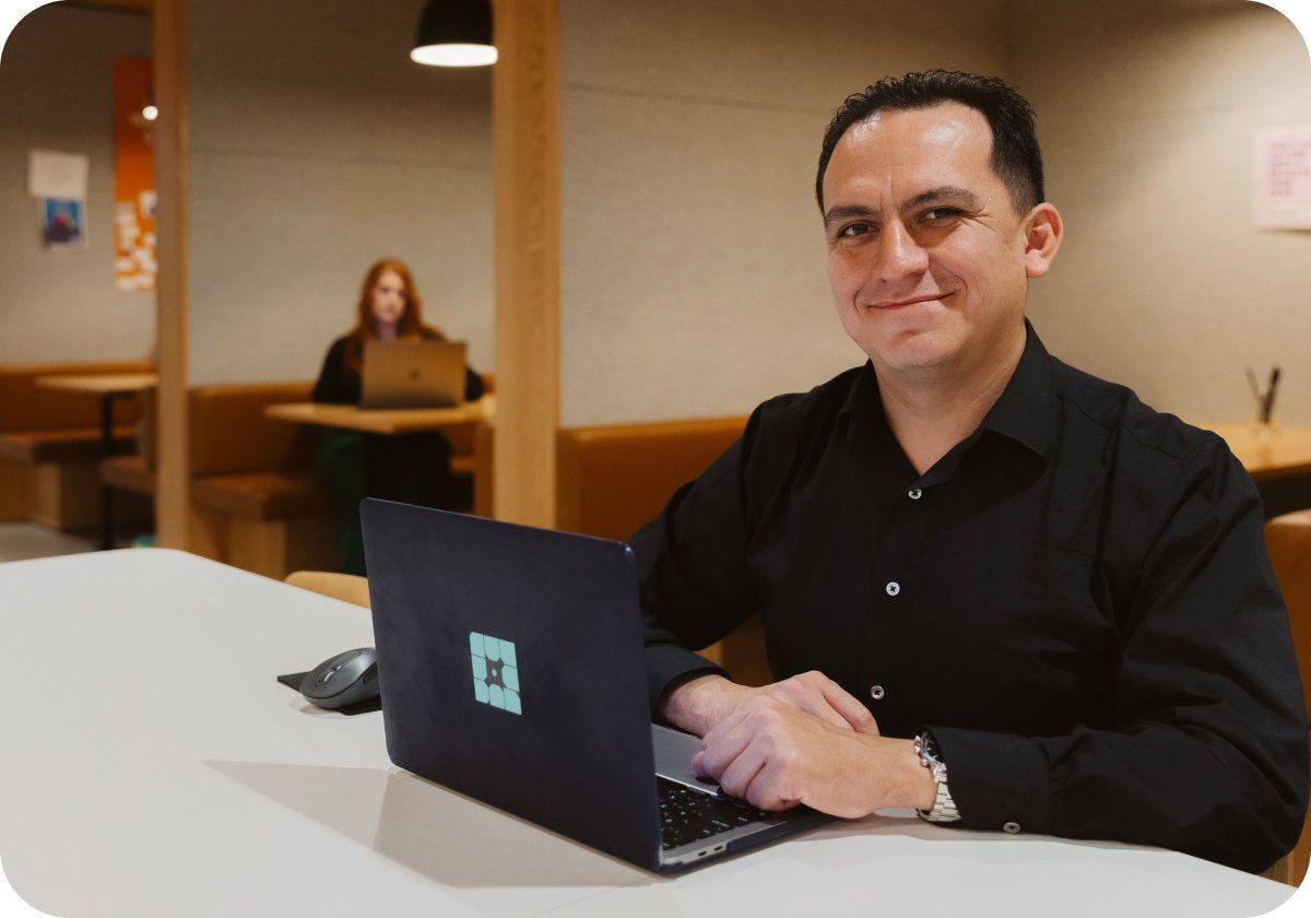 Man in black button-down shirt smiling with a laptop on his desk