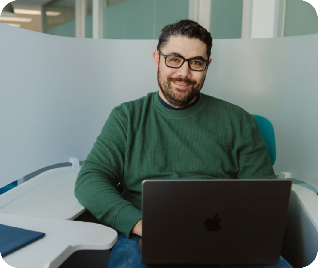 Man with glasses wearing a green turtleneck smiling with laptop