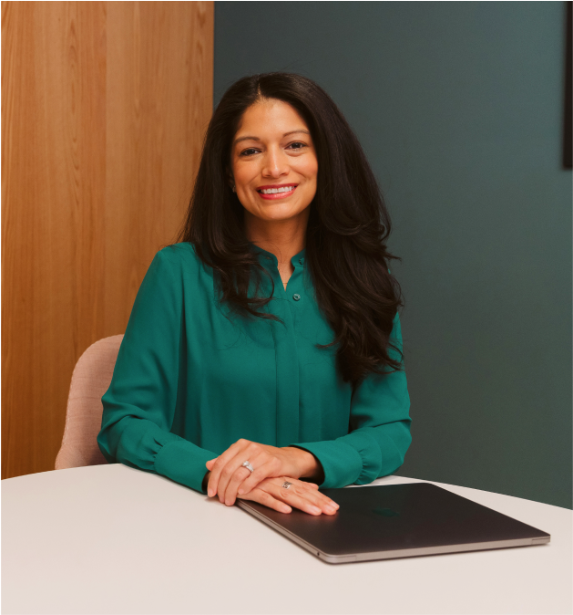 Business woman in green shirt sitting at a table with a closed laptop smiling.