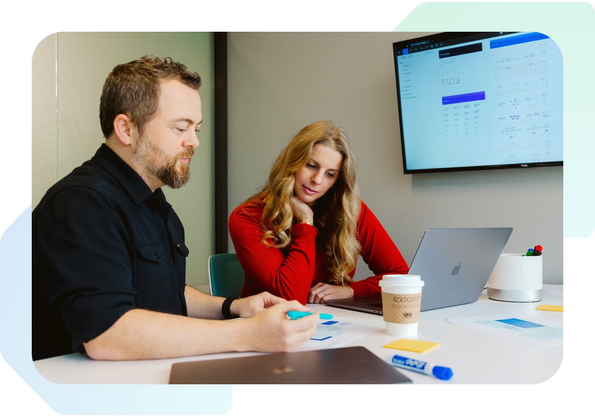 Coworkers working on a project in a meeting room with a monitor and laptop