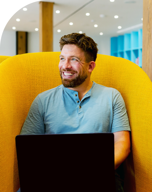 Man sitting on yellow couch with laptop smiling