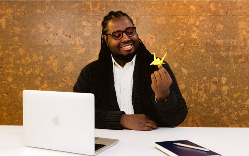 Happy man smiling with an open laptop and looking at an origami crane