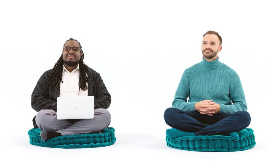 Two men sitting cross-legged on cushions looking relaxed