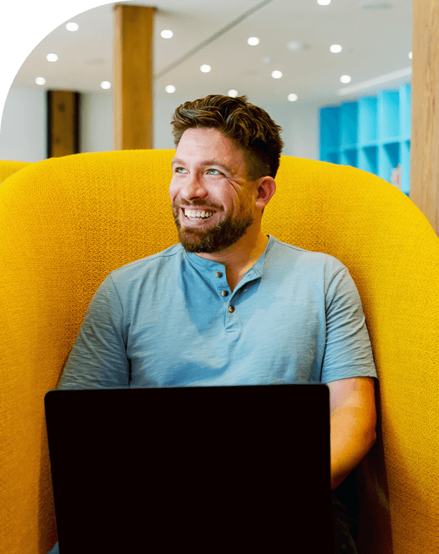 Man sitting on yellow couch with laptop smiling