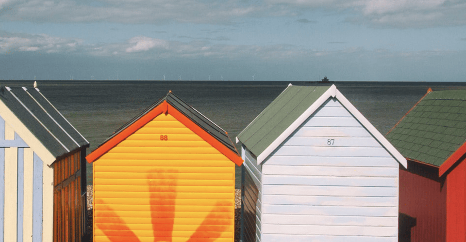 a row of sunny summer beach huts with different, vibrant paint colors
