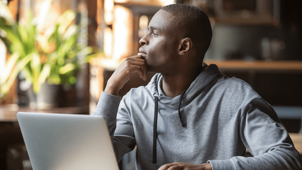 a man in a grey hoodie ponders a website design while seated in front of his laptop