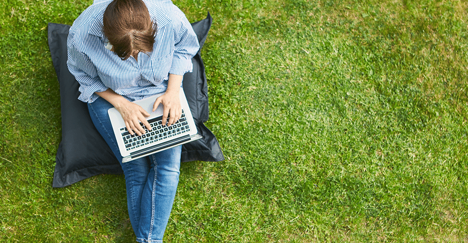 a woman works on a laptop outdoors in a large green space