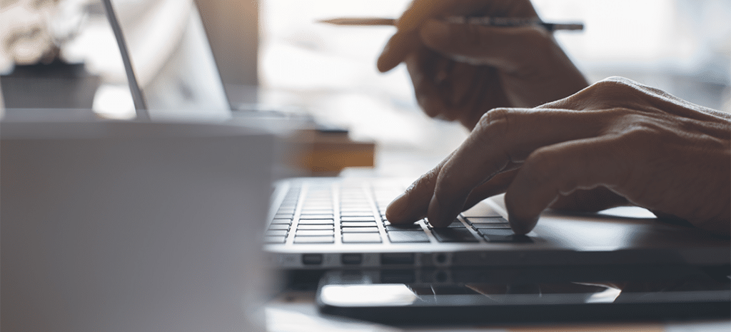 Person with one hand on laptop keyboard pencil in another hand