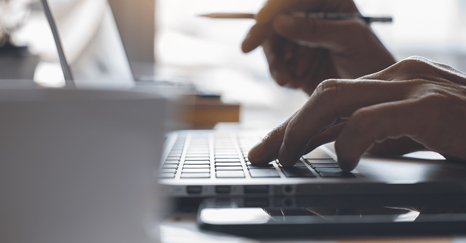 Person with one hand on laptop keyboard pencil in another hand