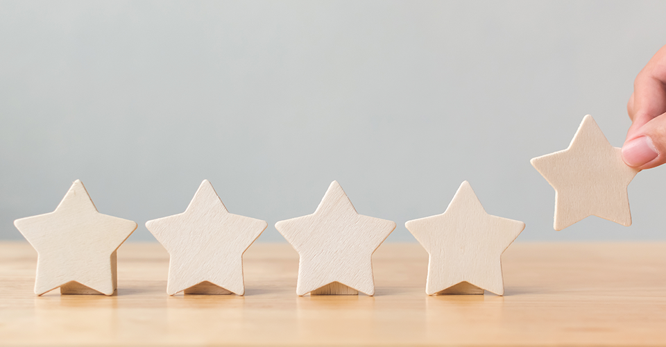 the secret to gaining customer loyalty. a hand places a fifth wooden star in a line of five stars