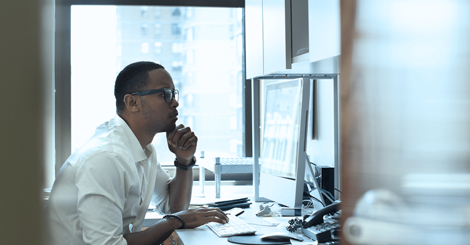 A man working in an office seated at a desk. Looking at a computer screen.