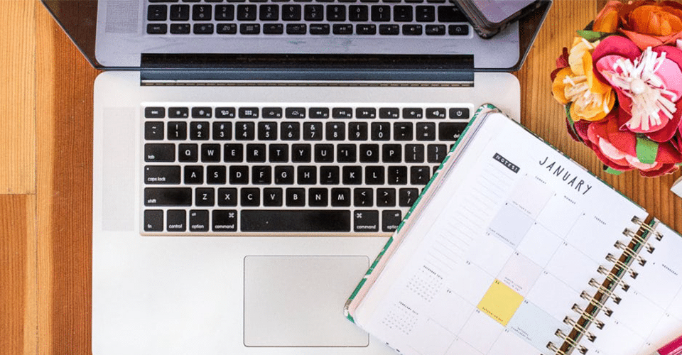 a laptop on a desk next to a monthly planner open to January