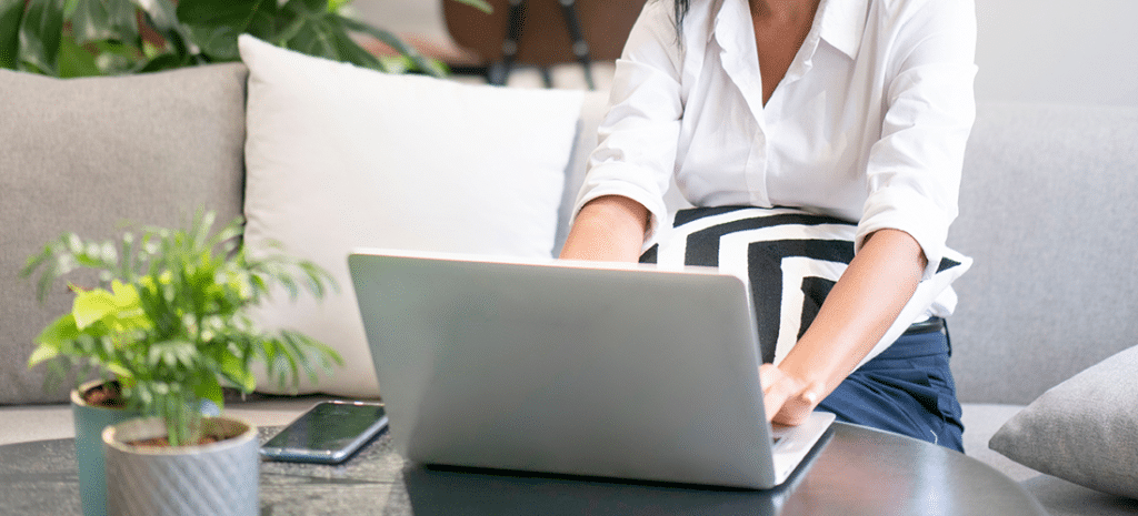 a woman works at a laptop next to a small plant