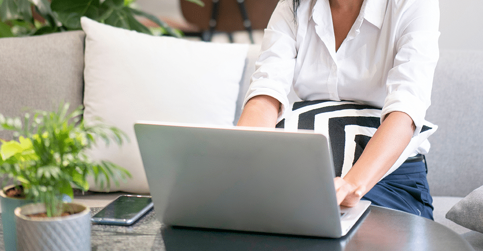a woman works at a laptop next to a small plant