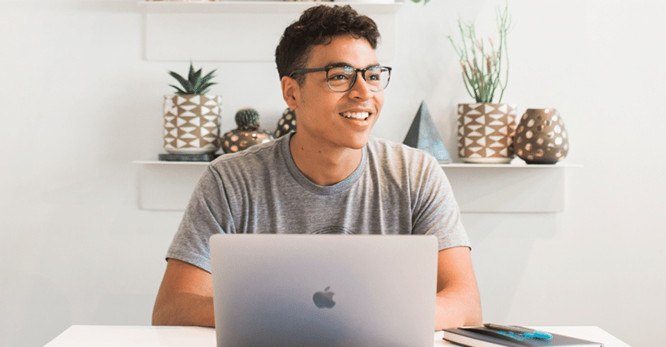 a man looks into the distance while sitting in a bright office space in front of a laptop