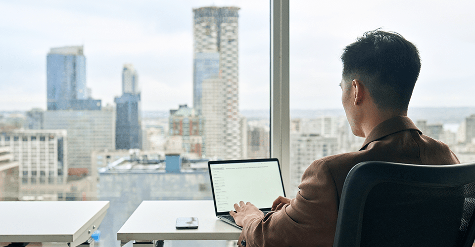 a man works on a laptop while looking out at the skyline of a large city
