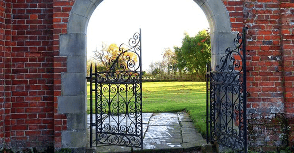 How to Utilize WordPress Gated Content on Your Website. An iron gate is positioned between the sides of an arch in a brick wall. The gate is open