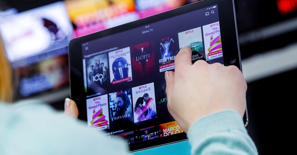 a person using a tablet views the thumbnails of potential shows or movies they can watch via a streaming platform