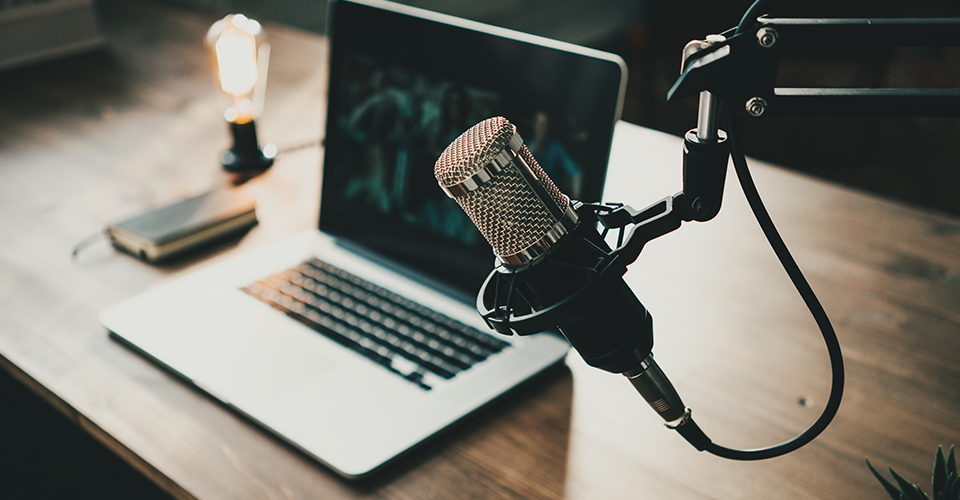 best marketing podcasts. Image shows an in-home podcast studio with a laptop , a light, and a microphone