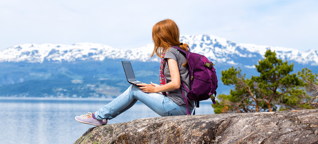 a travel blogger sits on a rock and writes down her thoughts in front of a mountain range