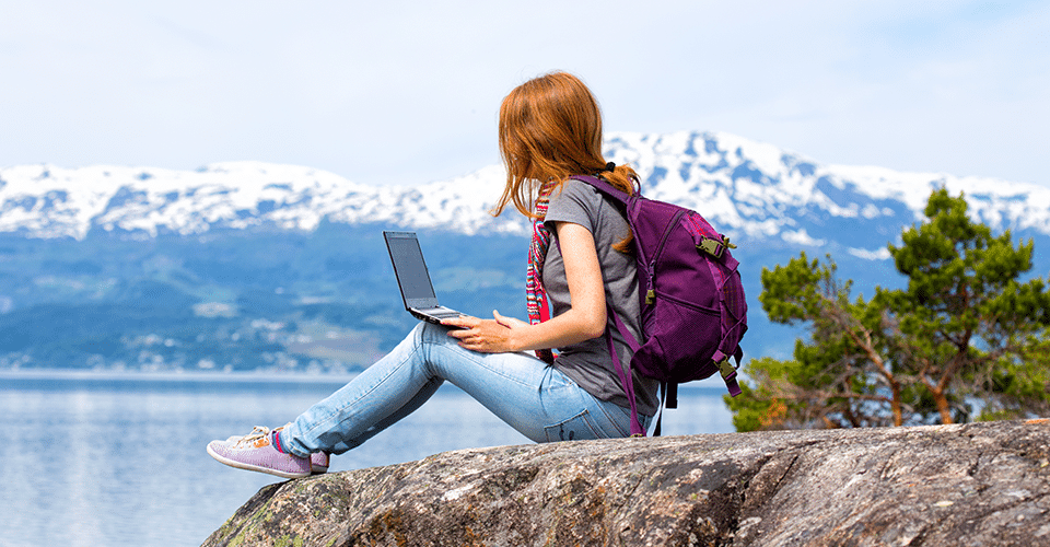 a travel blogger sits on a rock and writes down her thoughts in front of a mountain range