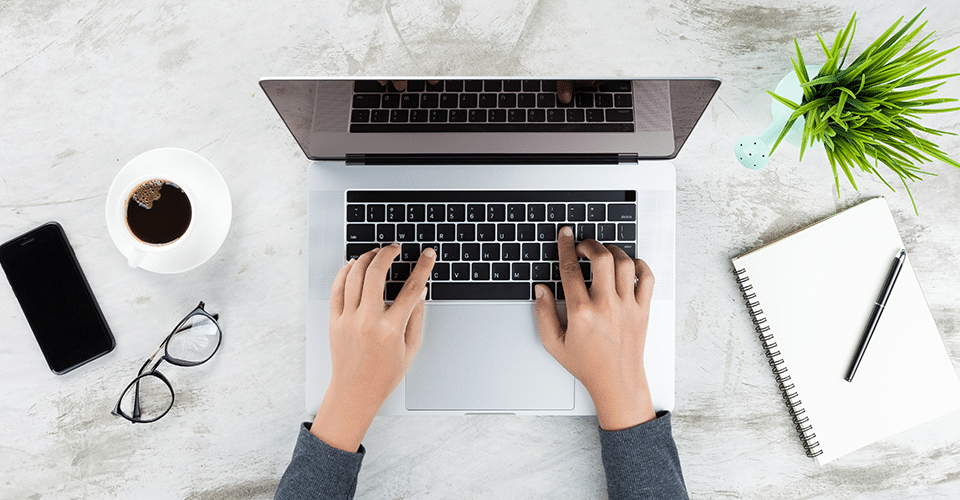 How to Add an Author Box to Your WordPress Posts. an author writes on a laptop next to a notebook and a coffee cup