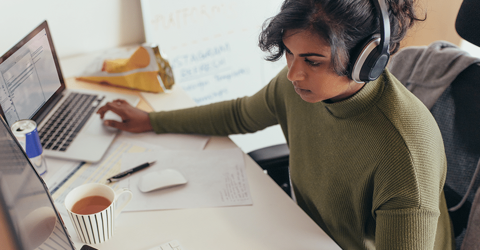 Programmer coding on a desktop computer and laptop at her desk in office.