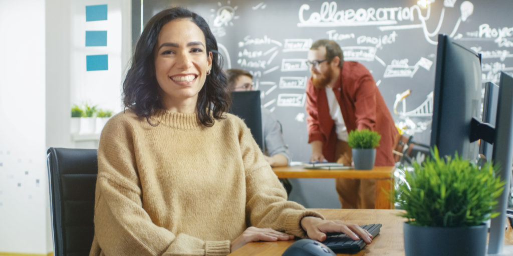 Woman Videographer Works on Her Personal Computer, Smiles on Camera.