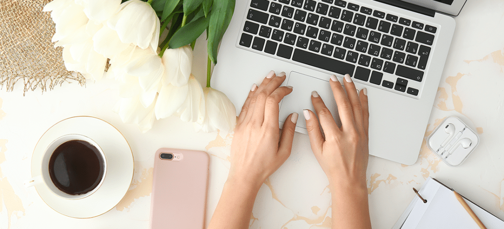 a woman works on a laptop at a desk next to flowers and a cup of coffee