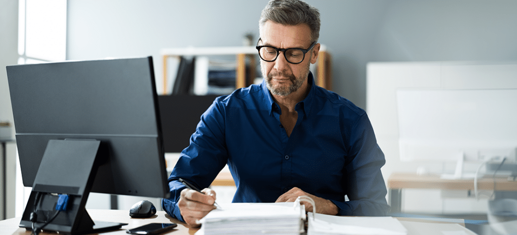 a businessman sits at a desk and looks over a stack of papers