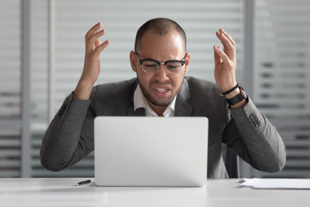 Angry stressed african business man using laptop mad about broken computer online problem annoyed with slow stuck laptop error, crazy about system virus or data loss, outraged with website mistake