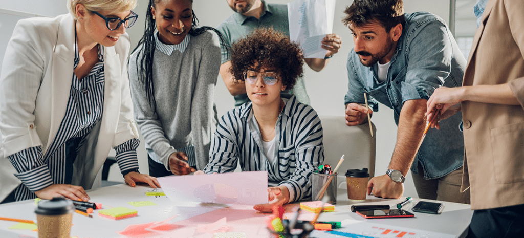 a group of creatives huddle around a woman holding a piece of paper as they all discuss a design