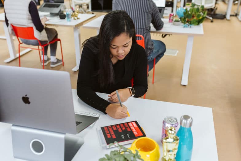a woman writes on a post it note as a reminder while sitting at a desk