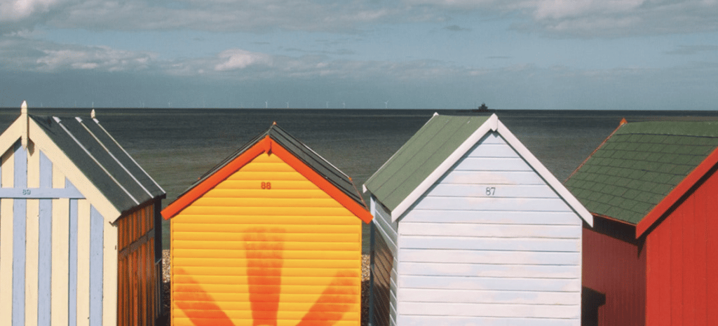 a row of sunny summer beach huts with different, vibrant paint colors