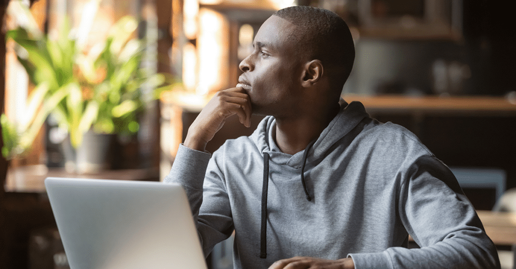 a man in a grey hoodie ponders a website design while seated in front of his laptop