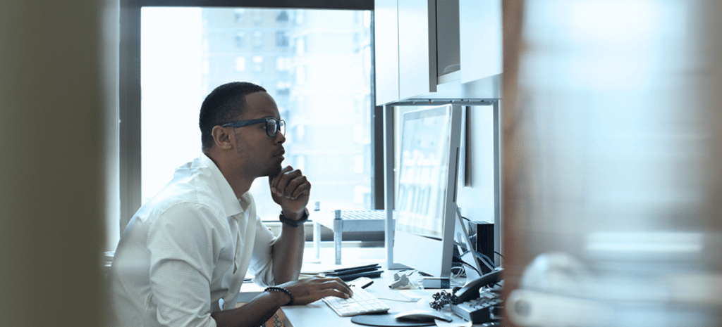 A man working in an office seated at a desk. Looking at a computer screen.