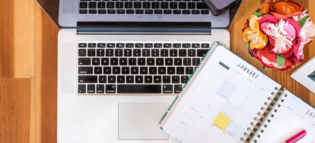 a laptop on a desk next to a monthly planner open to January