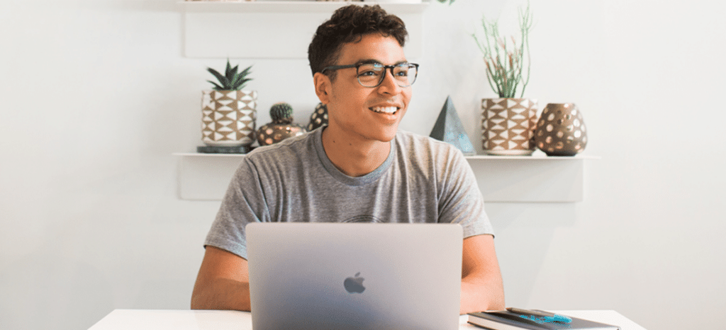 a man looks into the distance while sitting in a bright office space in front of a laptop