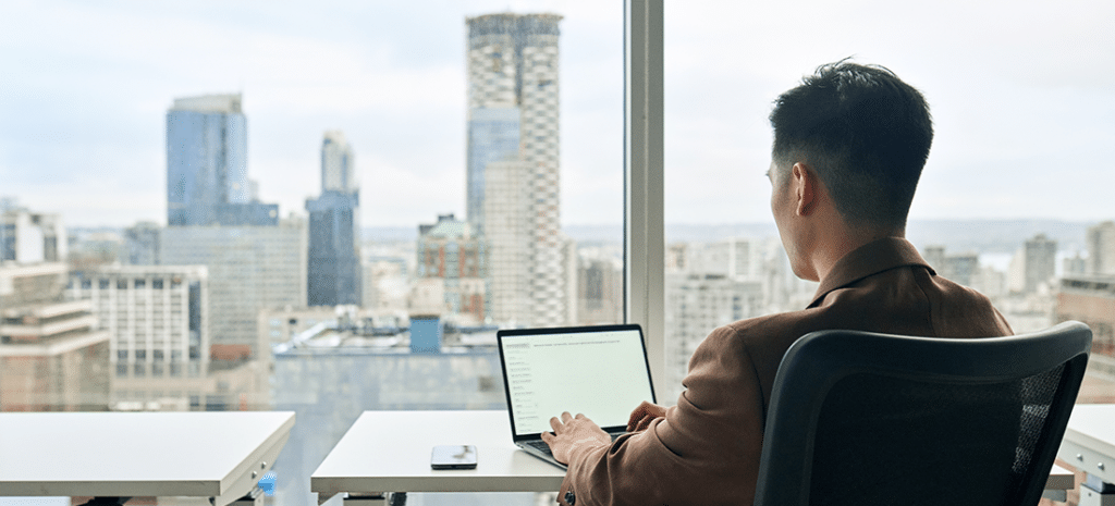 a man works on a laptop while looking out at the skyline of a large city
