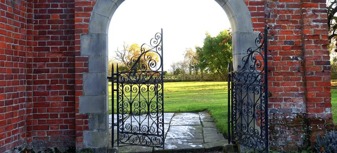 How to Utilize WordPress Gated Content on Your Website. An iron gate is positioned between the sides of an arch in a brick wall. The gate is open