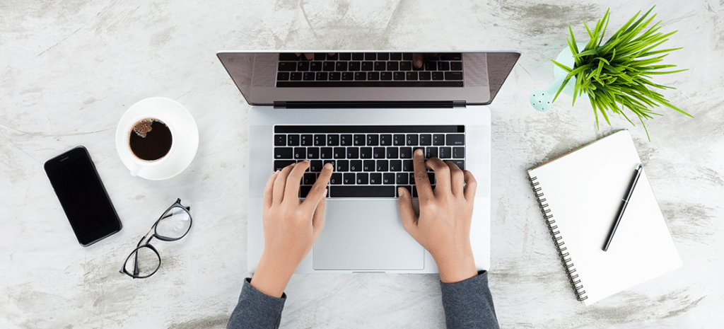 How to Add an Author Box to Your WordPress Posts. an author writes on a laptop next to a notebook and a coffee cup