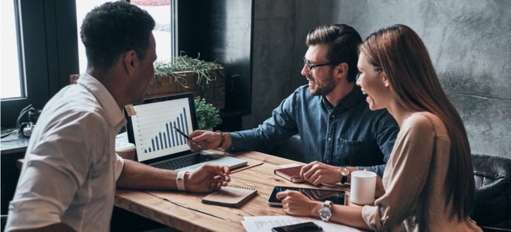 Group of young confident business people analyzing data using computer and smiling while working in the office