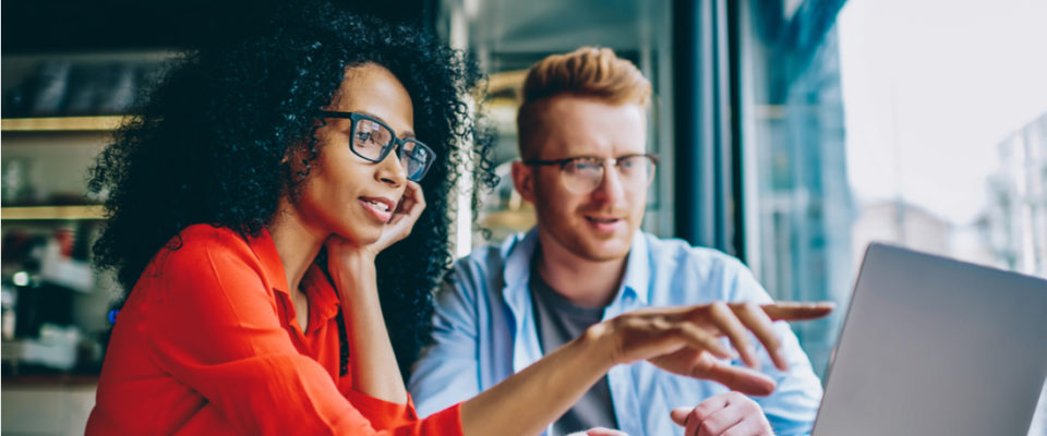 female graphic designer pointing with finger on laptop computer during collaboration with colleague