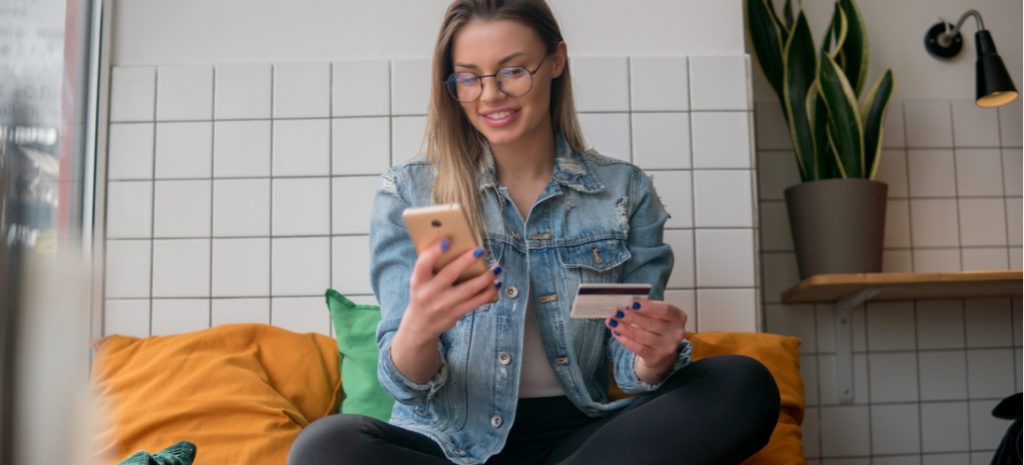 Photo of woman sitting comfortably using credit card to buy something on phone