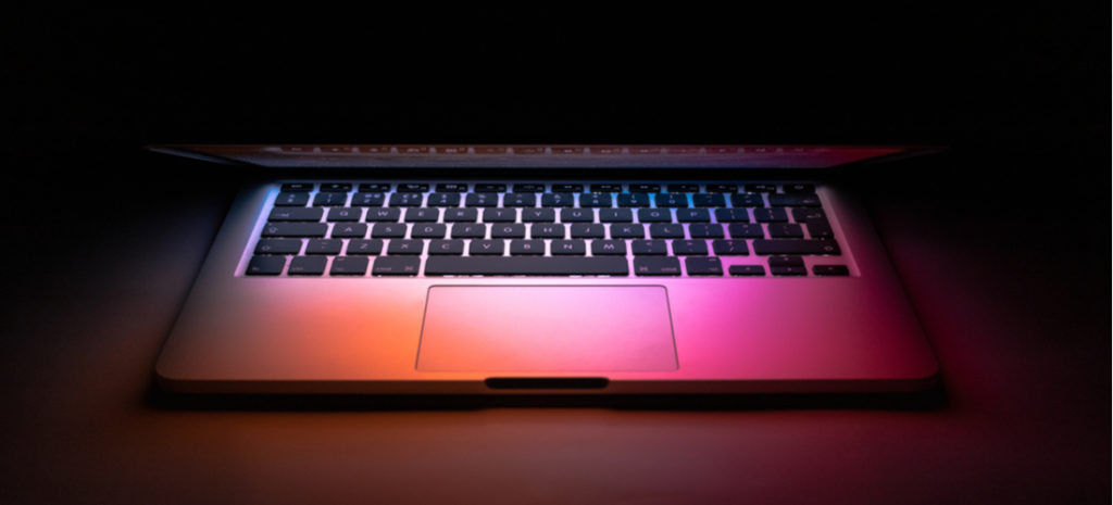 Image of Mac laptop in dark mode on desk with colorful light shining on keyboard