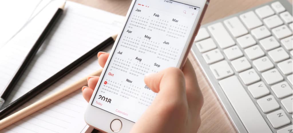 Person pressing phone calendar at desk with notebook and keyboard